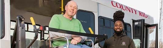 A man on a wheel chair being assisted off of a bus