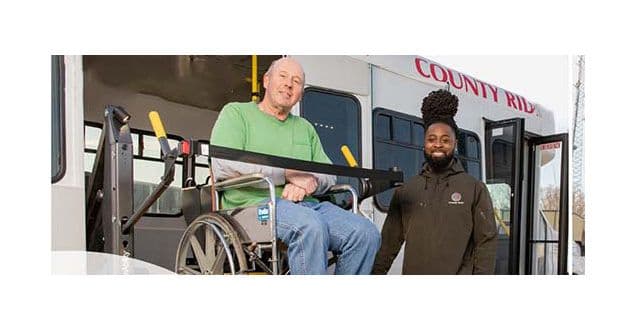 A man on a wheelchair being assisted off of a bus